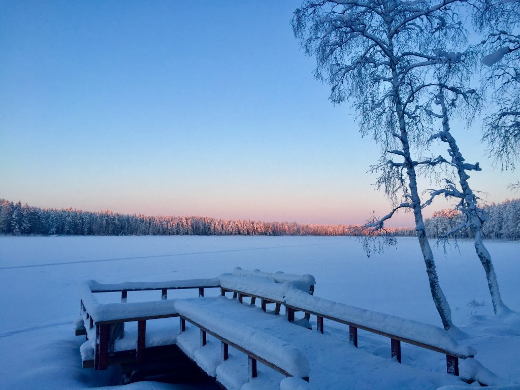 Ruuhijärven laituri talvella. Taustalla aurinko valaisee kaukaisia puiden latvoja.