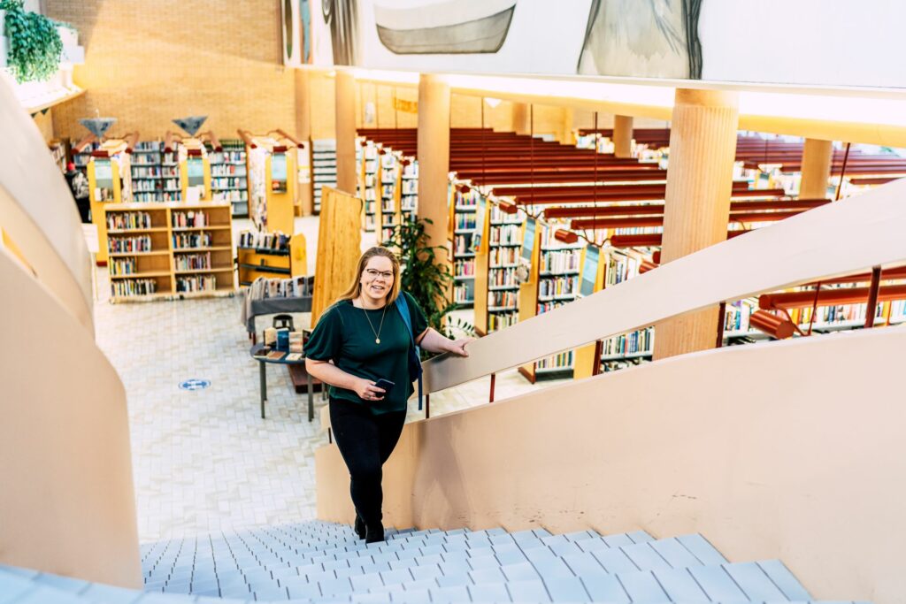 A smiling woman walks up the library stairs.